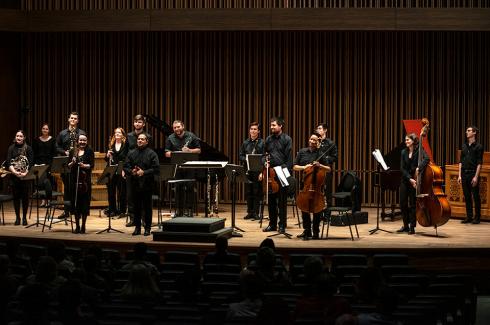 Sinfonietta stands on Pitzer Center stage, wearing all black, smiling, holding their instruments, and preparing to take a bow
