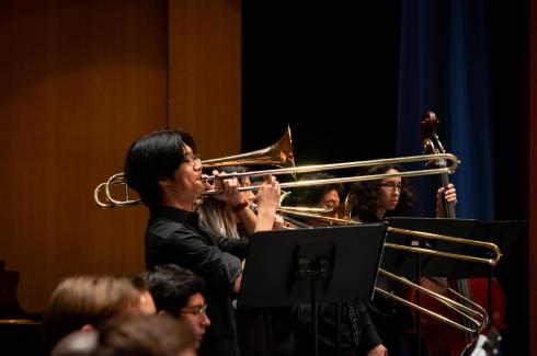 A trombonist with black hair stands playing his trombone towards the ceiling in the Mondavi Center.